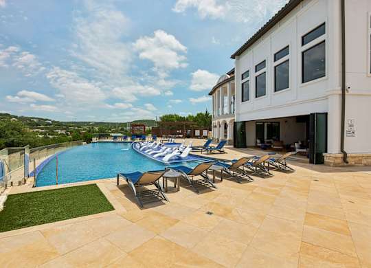 A pool with chairs and a building in the background.