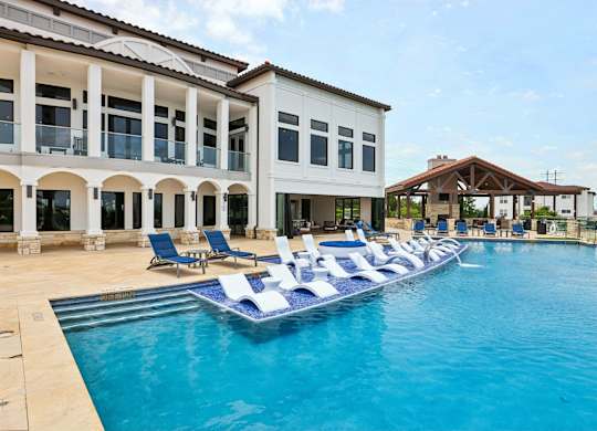 A large swimming pool with lounge chairs in front of a white building.