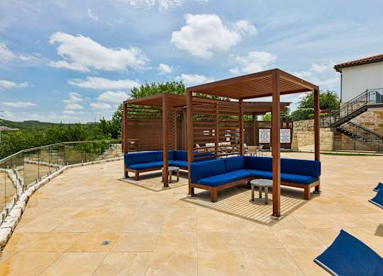 A wooden pavilion with blue seating is surrounded by a stone wall.