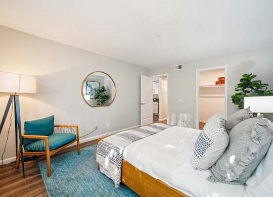 A bedroom with a bed, chair, and a mirror on the wall.