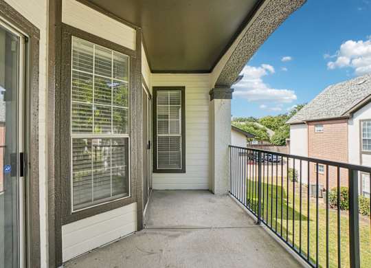 A balcony with a black railing and a view of a blue sky with clouds.