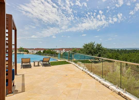 A pool area with a glass railing and chairs.