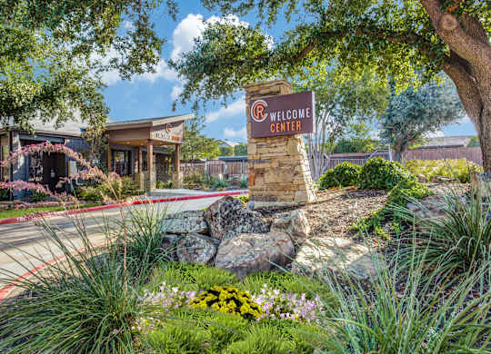 A welcome center sign is in front of a building with a landscaped area.
