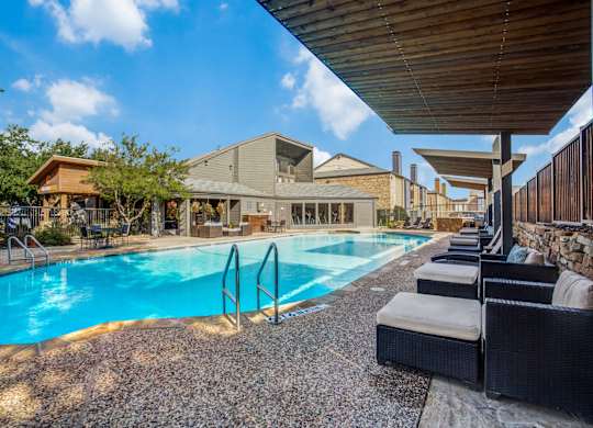 A large outdoor swimming pool with lounge chairs and a building in the background.