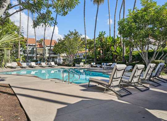 A pool surrounded by trees and chairs.