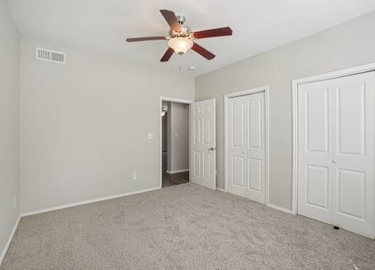A room with a ceiling fan and three doors.