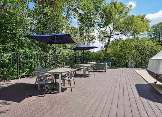 A wooden deck with chairs and tables is surrounded by green trees.