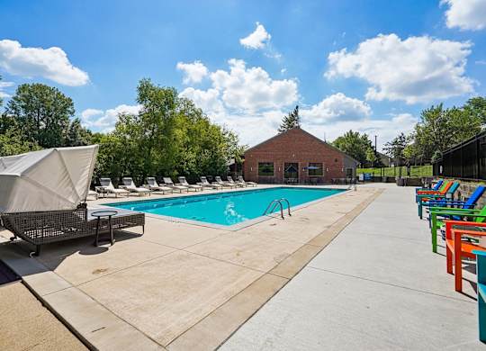 A pool area with a small building and lounge chairs.