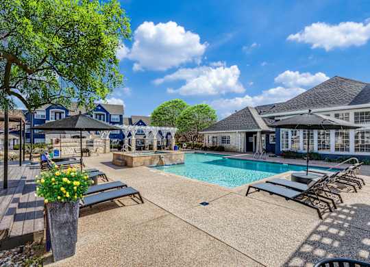 A pool area with sun loungers and a tree.