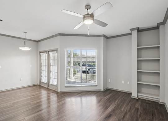 A room with a ceiling fan and a window with a view of a street.