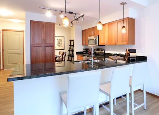 A kitchen with white chairs and a black counter top.