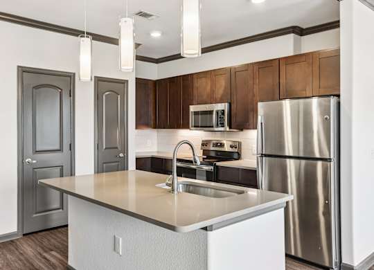A kitchen with a stainless steel refrigerator and a white island with a sink.