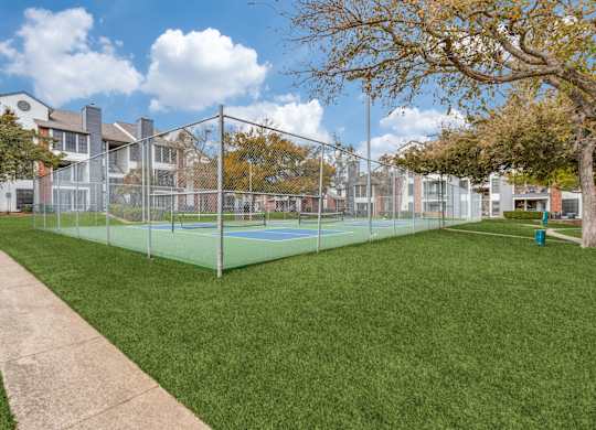 A tennis court is surrounded by a fence and a sidewalk.