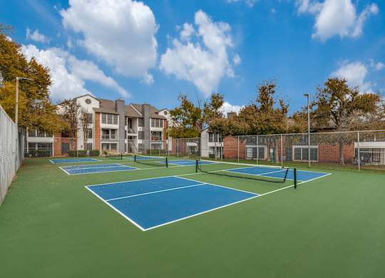 A tennis court surrounded by a fence and a building in the background.