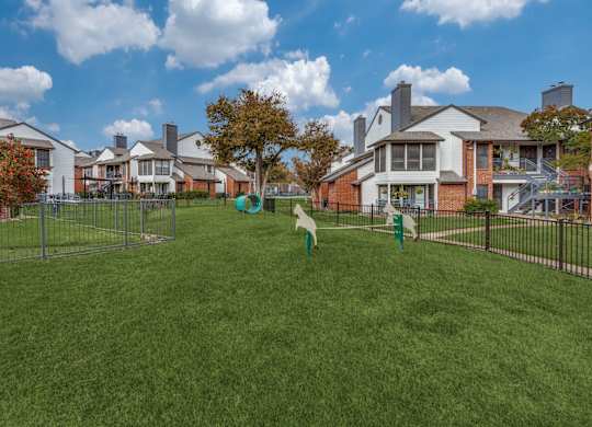A grassy field with a fence and houses in the background.