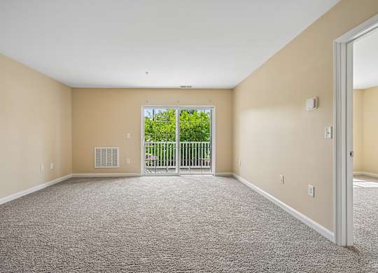 A spacious room with a carpeted floor and a sliding glass door leading to a balcony.