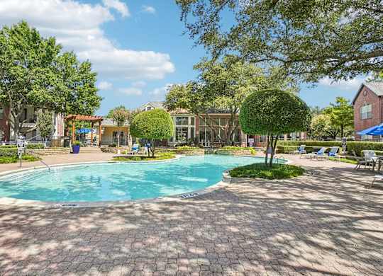 A pool surrounded by trees and a brick patio.