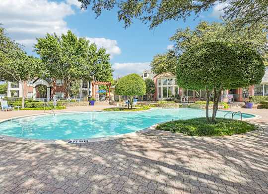 A swimming pool surrounded by trees and a brick patio.