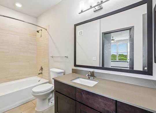 A bathroom with a white toilet, a white bathtub, and a large mirror.