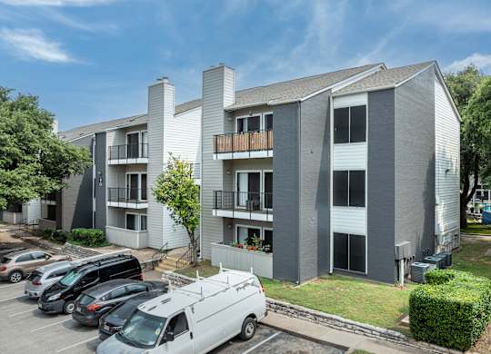 an image of an apartment building with cars parked in a parking lot
