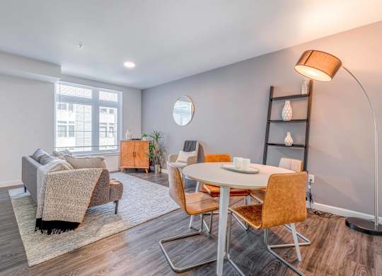 Studio Apartments in Green Lake Seattle WA - Circa Green Lake - Living Room with Couch, Area Rug, Dining Area, Wood-Style Flooring, and a Large Window.