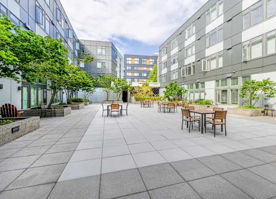 a courtyard with tables and chairs and trees and buildings in the background