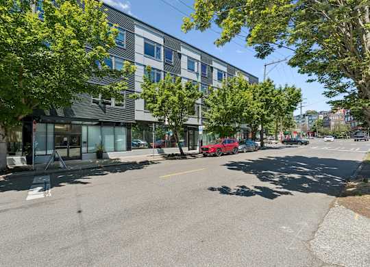 A street view with a building on the left and a red car on the right.