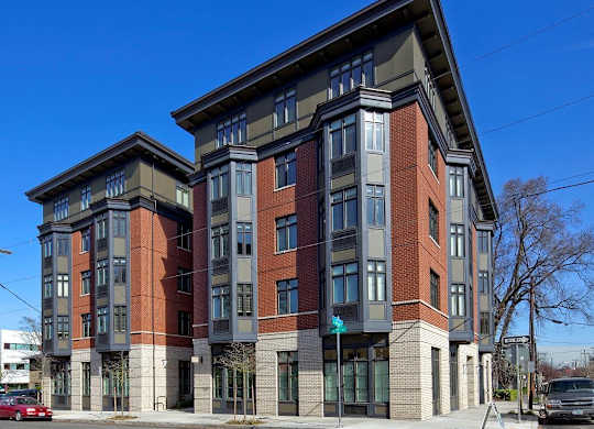A red car is parked on the street in front of a multi-story building.