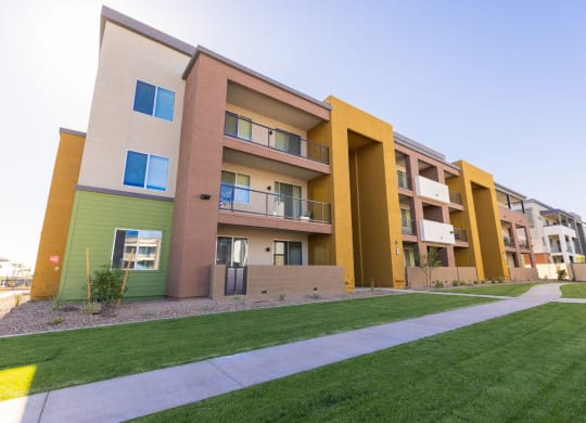 an exterior view of an apartment complex with green grass and a sidewalk