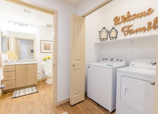 Three Bedroom Apartments in Gilbert AZ - Curve At Gilbert - Bathroom With Plank Flooring, Wood-Inspired Cabinets, A Large Vanity Mirror, And A Full-Sized In-Unit Washer And Dryer