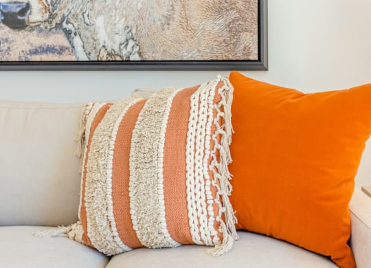 a white couch with an orange pillow and a painting of a cow