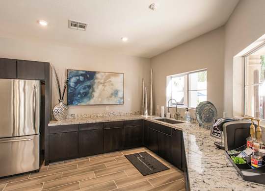 Apartments in Ahwatukee, AZ - Pacific Bay Club - Kitchen with Tiled Floor, Stainless Steel Appliances, Granite Countertops, Dark Wood Cabinetry, Windows, and Framed Artwork.