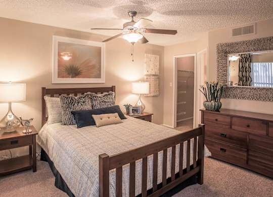 Apartments Ahwatukee, AZ - Pacific Bay Club - Bedroom with Carpeted Flooring, Bed, Wooden Nightstands with Lamps, Dresser, Framed Mirror, Ceiling Fan, and Large Closet.