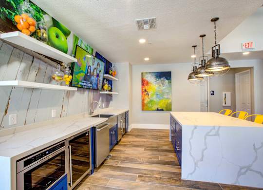 Apartments for Rent in North Phoenix, AZ - Ironhorse at Tramonto - Resident Lounge with a Kitchen, Floating Display Shelves, Wall-Mounted TV, Large Granite Kitchen Island with Seating, and Hanging Light Fixtures.