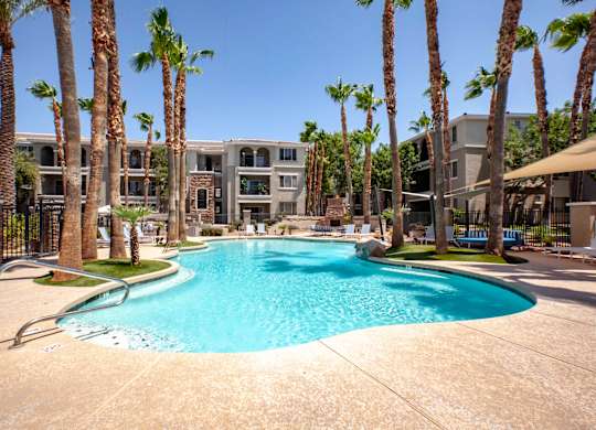 North Phoenix AZ Apartments - Ironhorse at Tramonto - Gated Resort-Style Pool with Lounge Chairs, Umbrellas, Palm Trees, Landscaping, and Building Exterior in Background