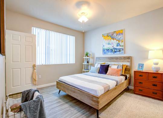 1 Bedroom Apartments in North Phoenix - Ironhorse at Tramonto - Bedroom with Wood-Style Flooring, Area Rug, Bed, Dresser/Nightstand, Lamps,Hamper, Storage Rack, and Large Window