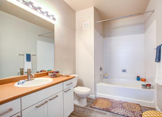 Pet-Friendly Apartments in North Phoenix, AZ - Ironhorse at Tramonto - Bathroom with Vinyl Plank Flooring, Orange Quartz Countertop, Spacious Vanity Mirror, and Shower/Tub Combo.