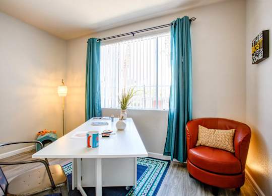 2-Bedroom Apartments in North Phoenix, AZ - Ironhorse at Tramonto - Study Area with Vinyl Plank Flooring, Area Rug, Desk with Chair, Red Armchair, Floor Lamp, and Large Window.