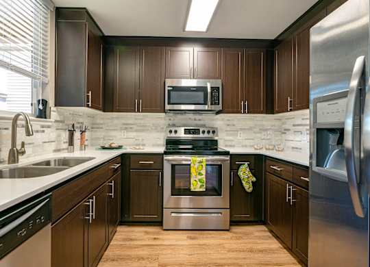 Walnut Creek, CA, Apartments - Ivy Hill - Kitchen with Hardwood Floor, Stainless Steel Appliances, Tile Backsplash and White Countertops, and Large Window above Double Sink.