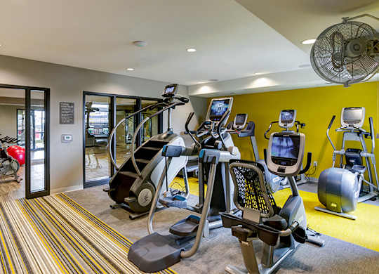 a gym with cardio equipment and weights in a building with yellow walls