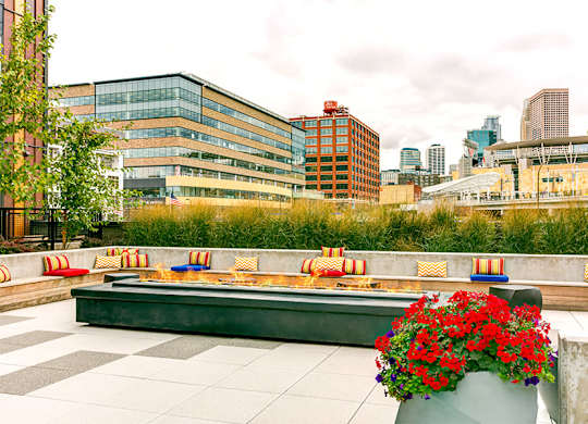 A patio with a bench and a planter with red flowers.