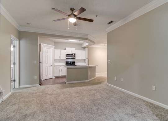 Woodstock, GA Apartments – Lea Woodstock – Living room with plush carpeting, ceiling fan and view of kitchen