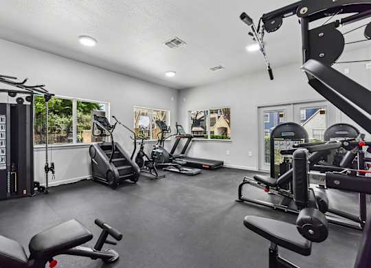 A spacious gym with various exercise equipment and a view of trees outside the windows.