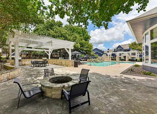A patio with a fire pit and chairs under a pergola.
