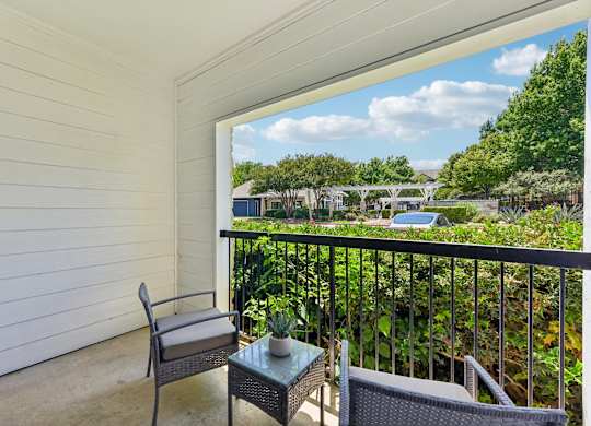 A balcony with a chair and table overlooking a green landscape.