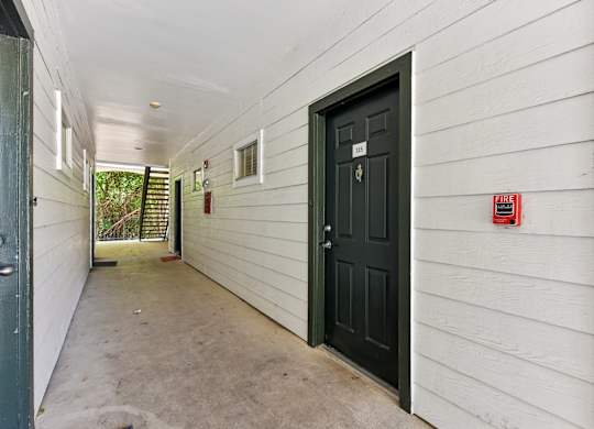 A hallway with a black door and a fire extinguisher on the wall.