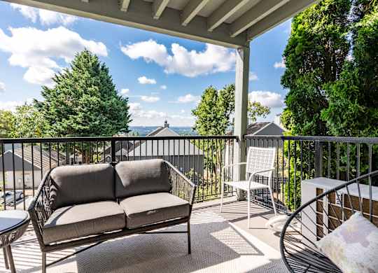 Mountain Park OR Apartments for Rent - MiLO at Mountain Park - Private Balcony with Patio Furniture and an Area Rug, Surrounded by a View of Trees and the Apartment Building.