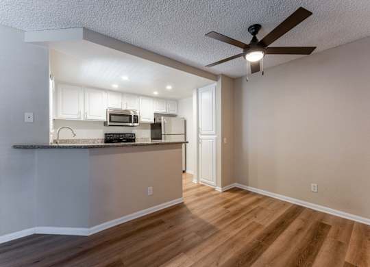 an empty living room and kitchen with a ceiling fan