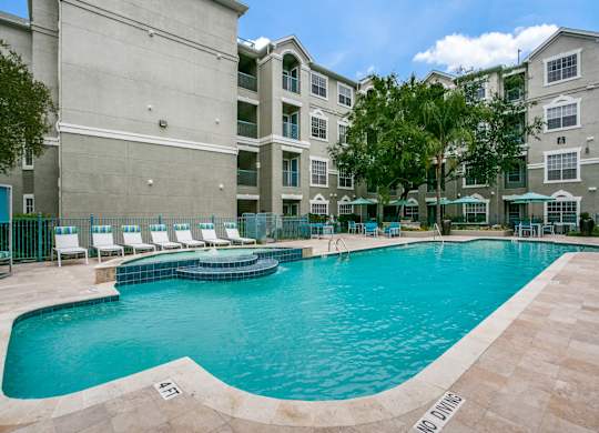 Houston Apartments for Rent - Large Enclosed Community Pool with Lounge Seating Surrounded by Greenery