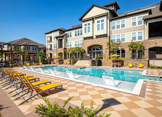 A large swimming pool with lounge chairs in front of a building.